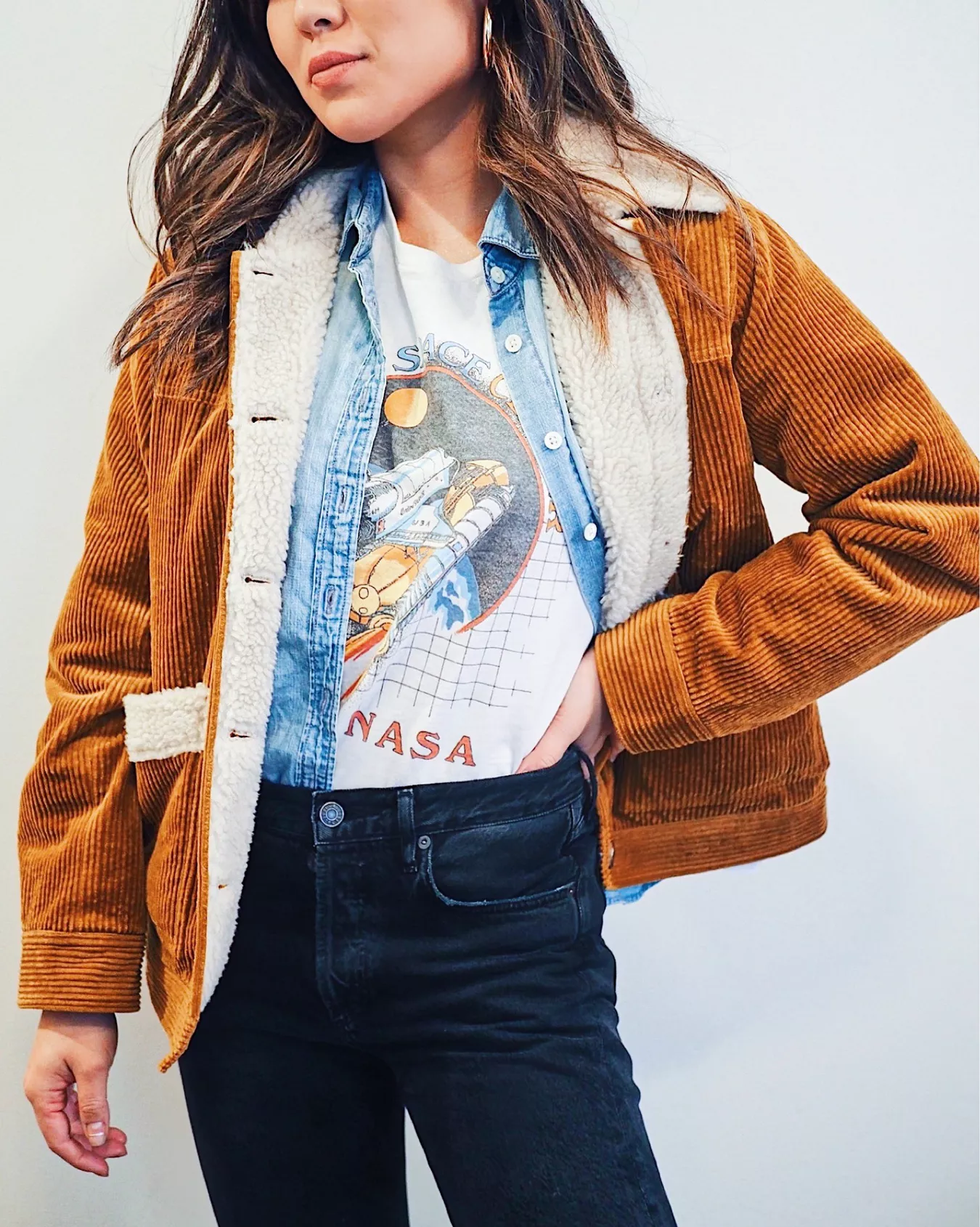 Woman wearing a caramel corduroy sherpa-lined jacket, denim shirt, NASA graphic tee and black mom jeans