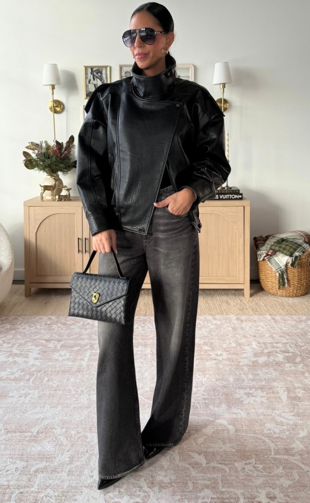 Woman wearing a black leather moto jacket with dark wide-leg jeans and a quilted handbag