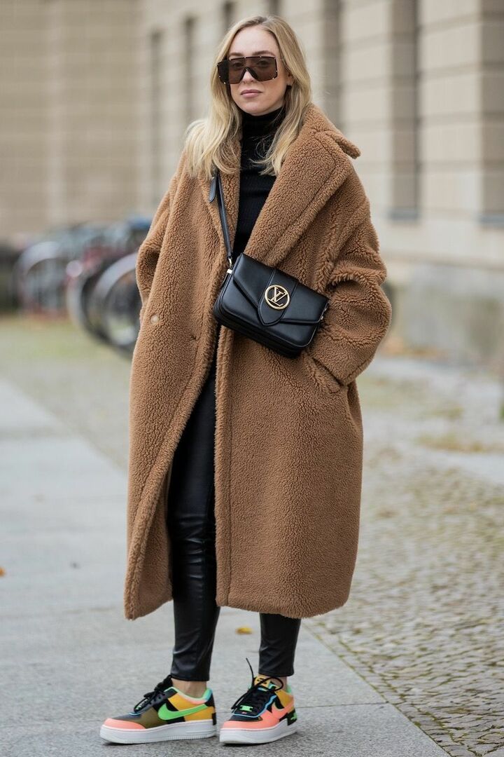 Woman in an oversized camel teddy coat with leather leggings, colorful sneakers and sunglasses