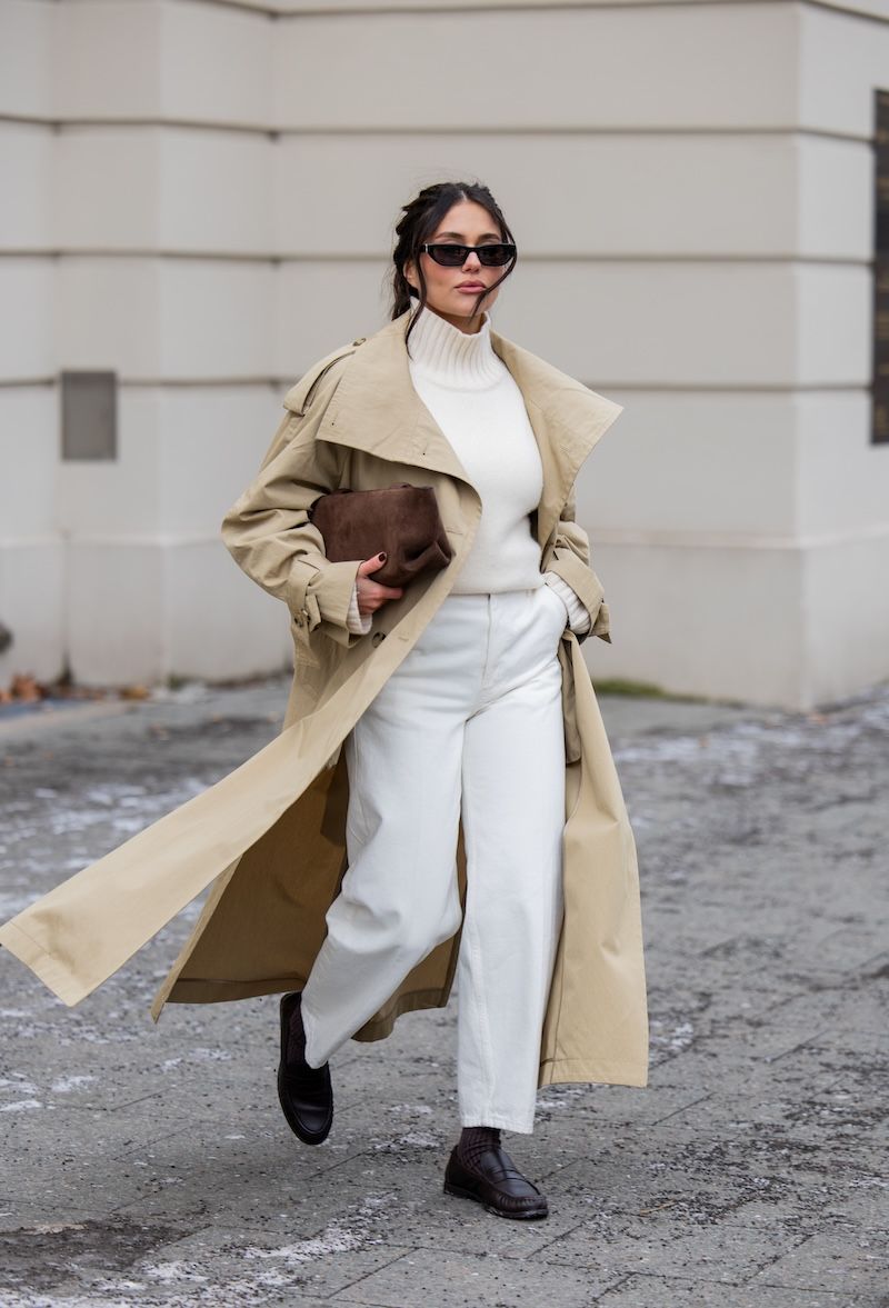 Woman in a beige trench coat with a cream turtleneck, white wide-leg trousers and loafers