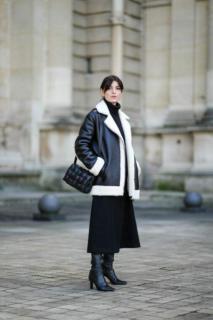 Woman wearing a black shearling-trim leather jacket with a black turtleneck and black midi skirt