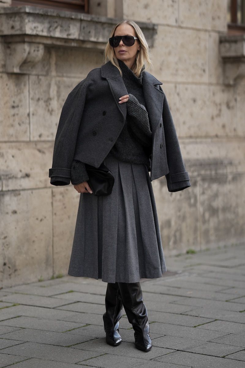 Woman wearing a charcoal peacoat with a gray pleated midi skirt and black knee-high boots