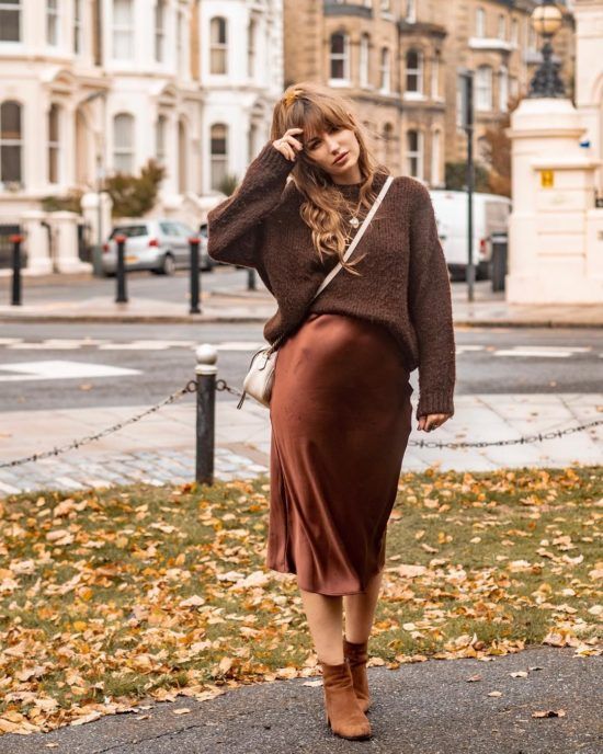 Woman in a chocolate brown satin midi skirt, chunky brown knit sweater and tan ankle boots