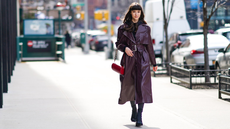 Wine-colored faux-leather trench coat styled with a red handbag on a city street