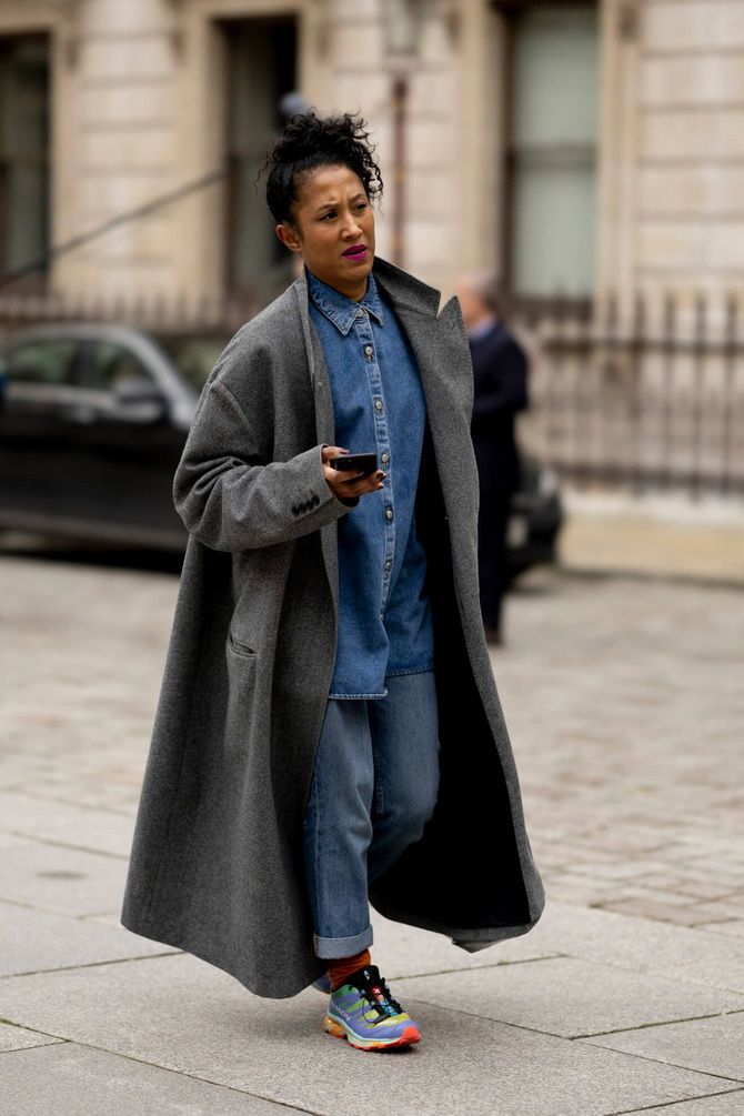Woman in a long grey wool coat layered over a denim shirt and jeans, street style