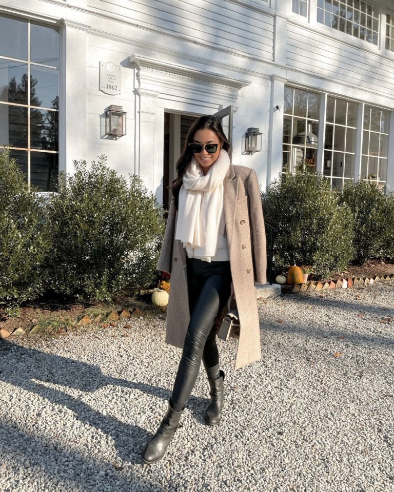 Woman in a camel wool coat with a cream scarf, black top, black leather leggings and ankle boots