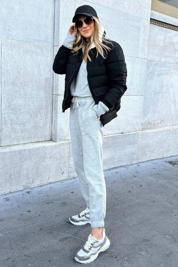Woman in a black puffer jacket with a gray sweatsuit, sneakers and a cap