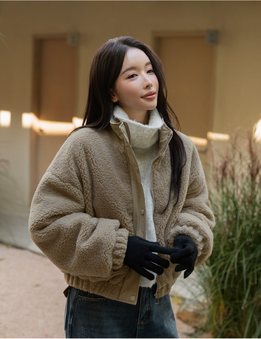 Woman in a taupe sherpa bomber fleece with a white turtleneck and black gloves