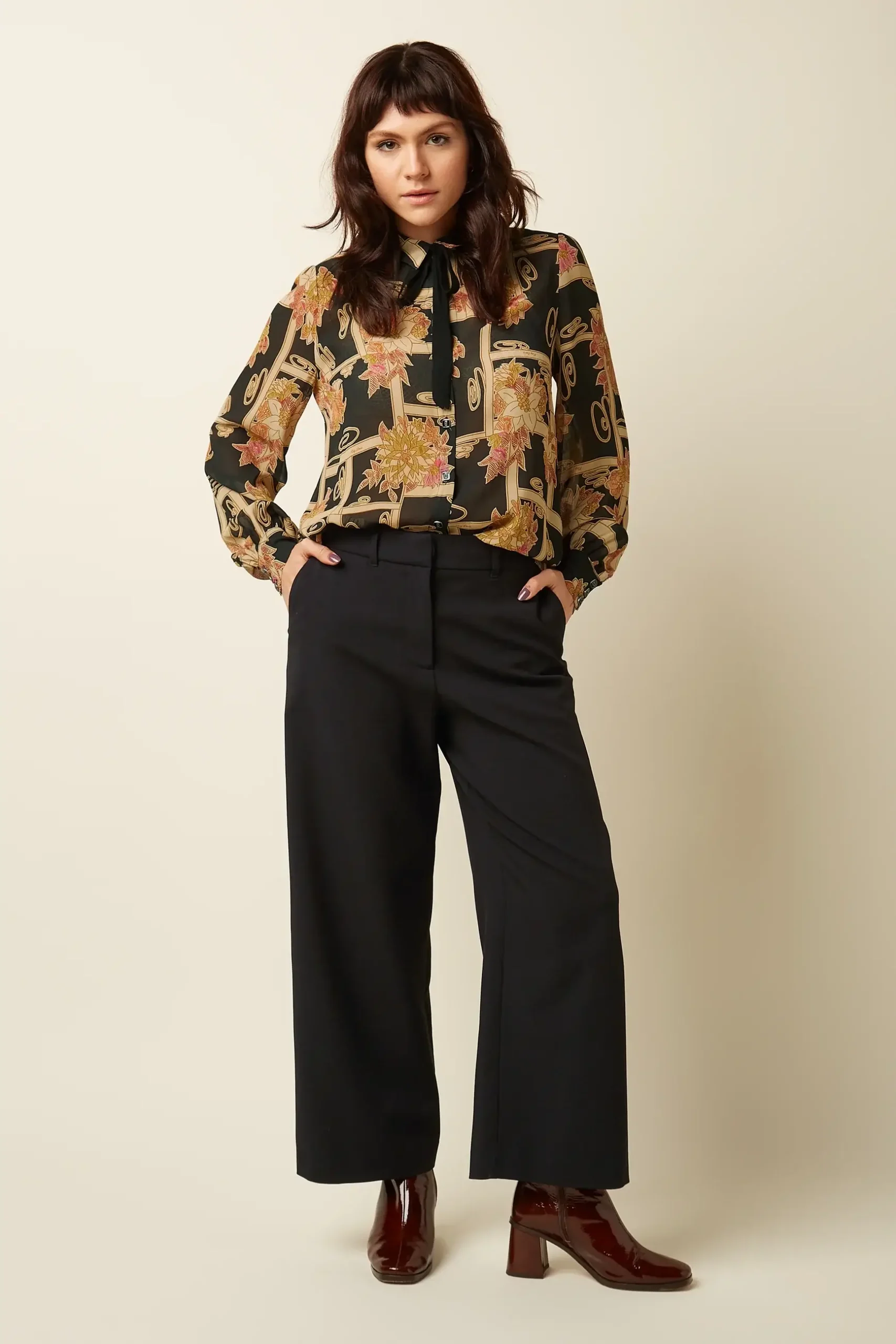 Woman wearing a black floral print blouse, black wide-leg trousers and burgundy patent ankle boots