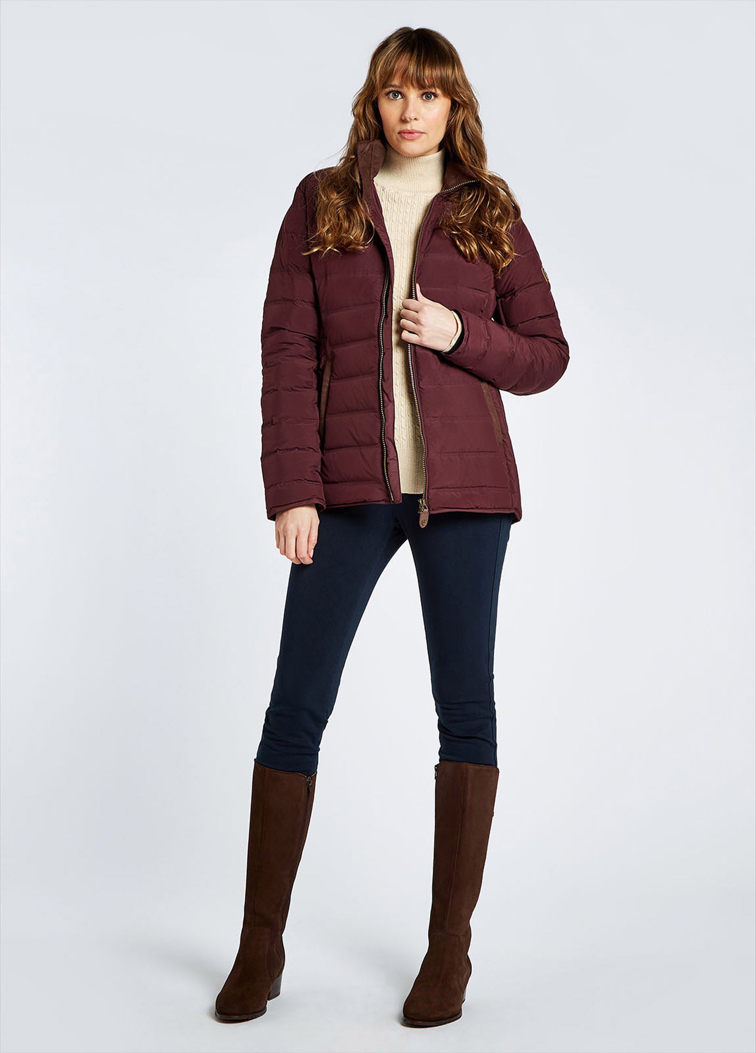 Woman in a burgundy down jacket with a cream turtleneck sweater, dark leggings and brown knee-high boots