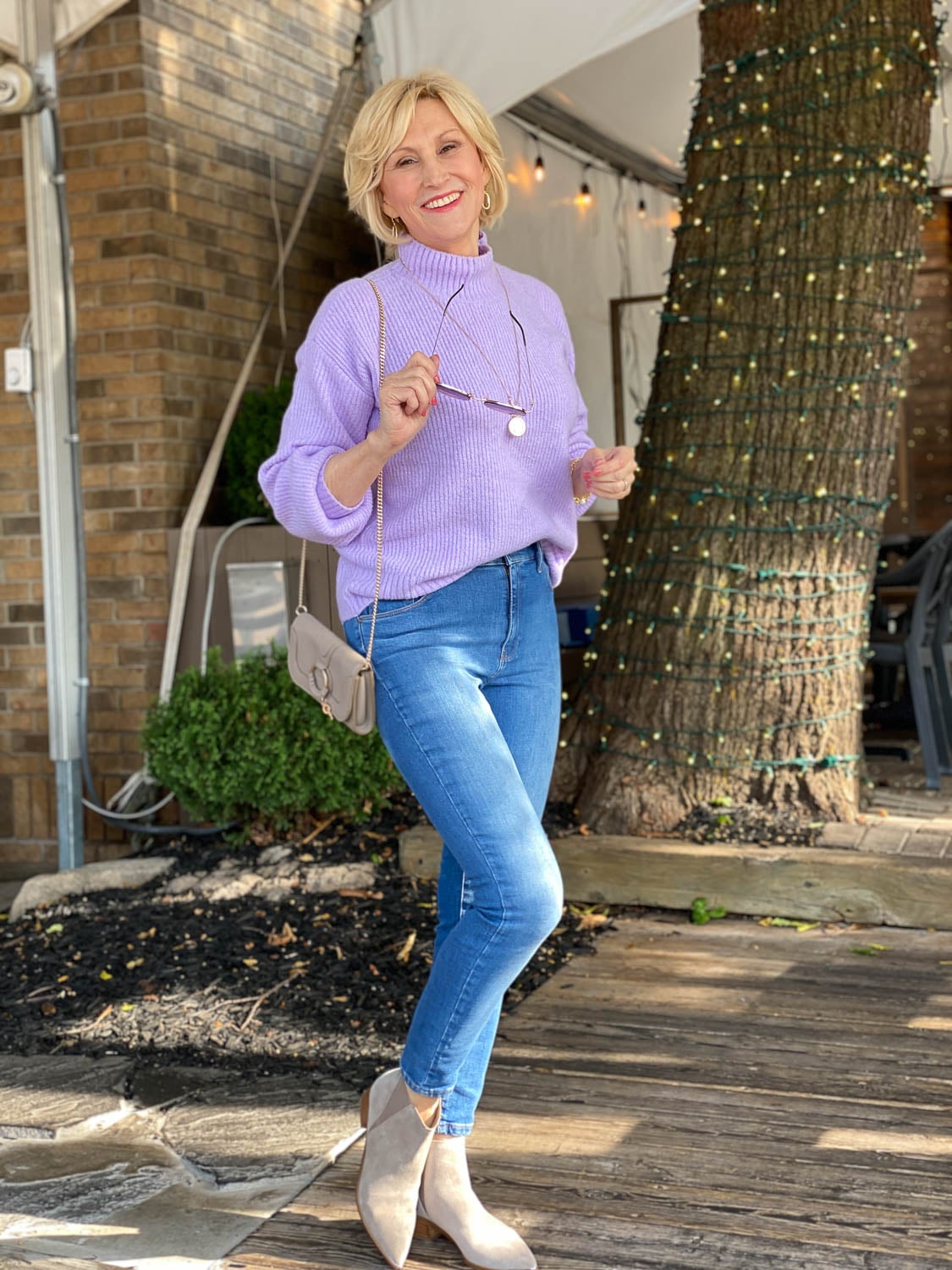 Woman in a lilac ribbed turtleneck sweater with blue jeans and taupe ankle boots