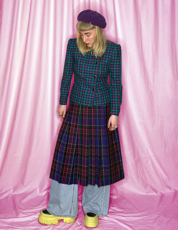 Woman wearing a green and purple tartan blazer with a matching long tartan pleated midi skirt and a purple beret