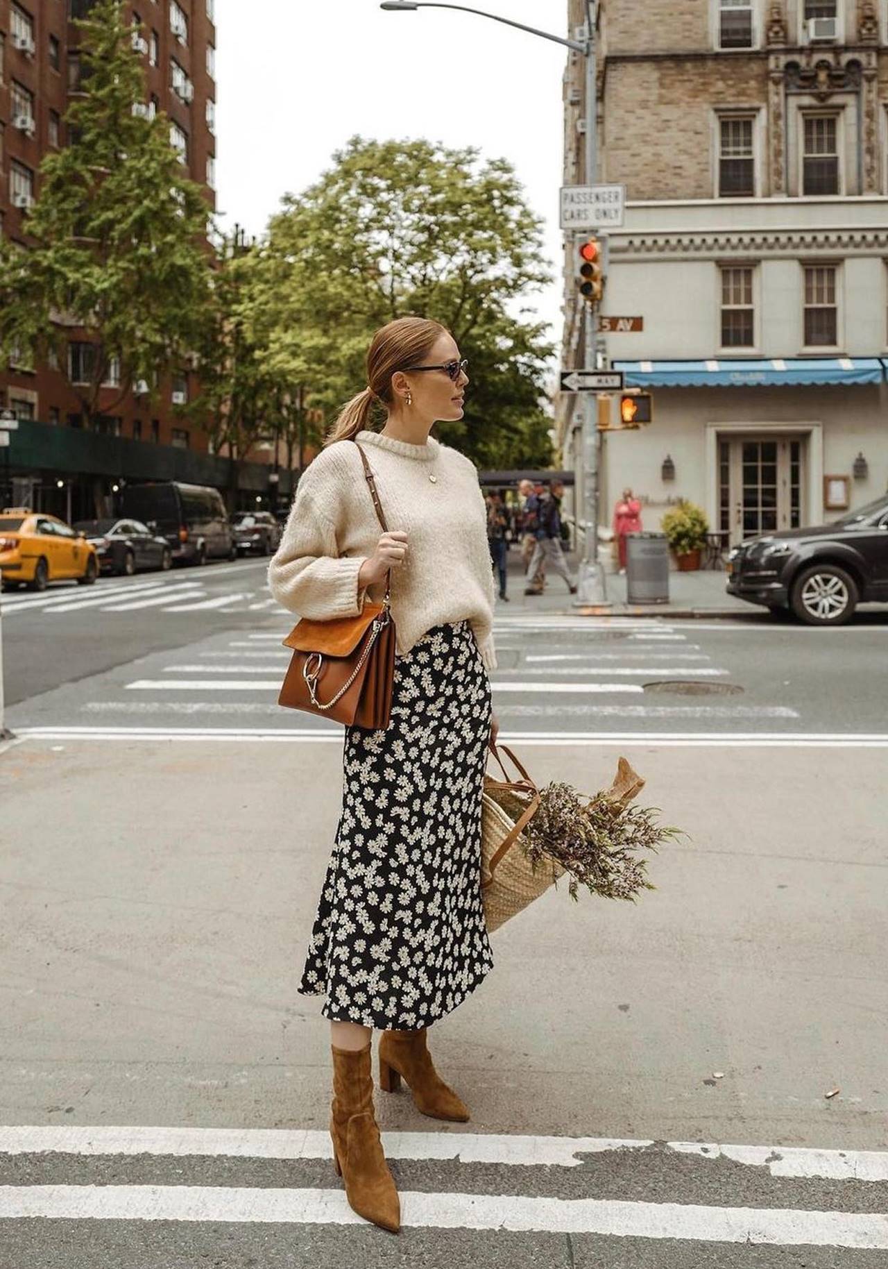 Woman in tan suede ankle boots, cream chunky knit sweater and a black floral midi skirt