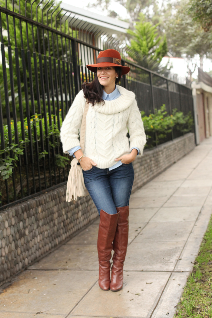 woman in white cable-knit sweater, rust fedora and cognac riding boots