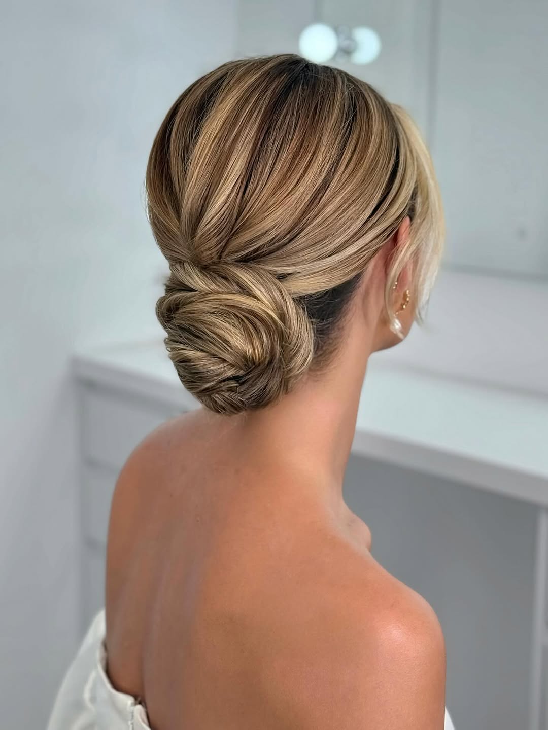 Twisted low knot bun with smooth finish in blonde balayage hair
