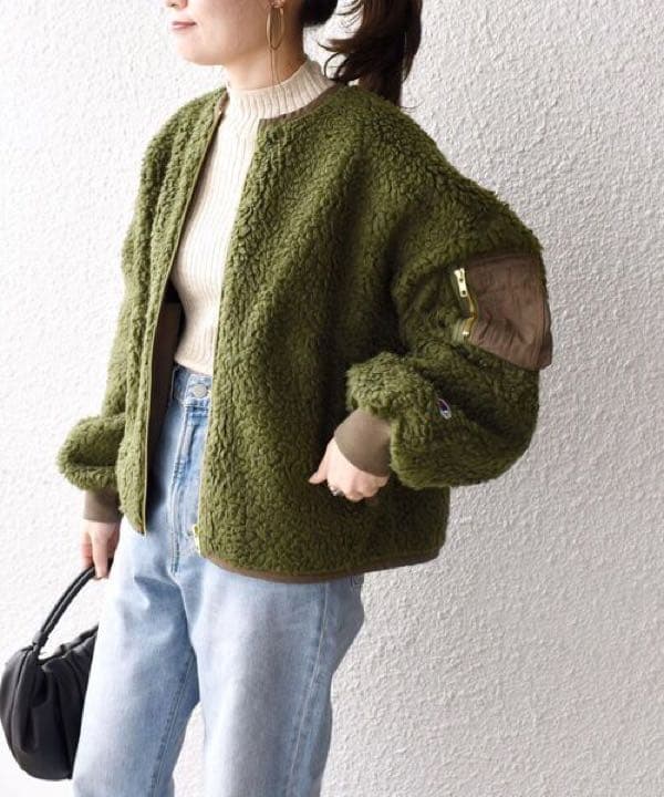 Woman in an olive sherpa bomber-style fleece with a cream knit and light-wash jeans
