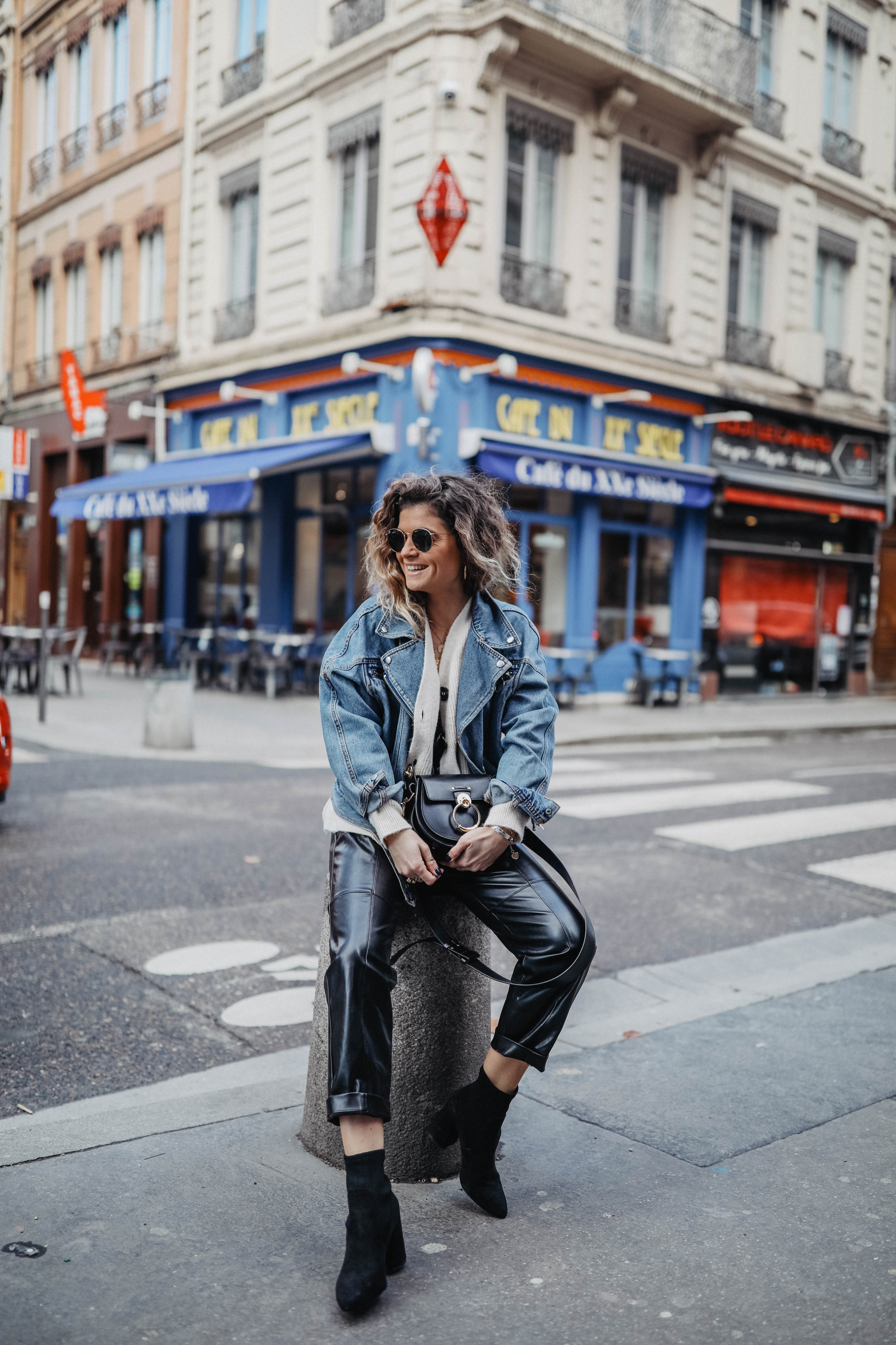 Woman in an oversized denim jacket and cream knit with cuffed black leather jogger pants and black sock boots
