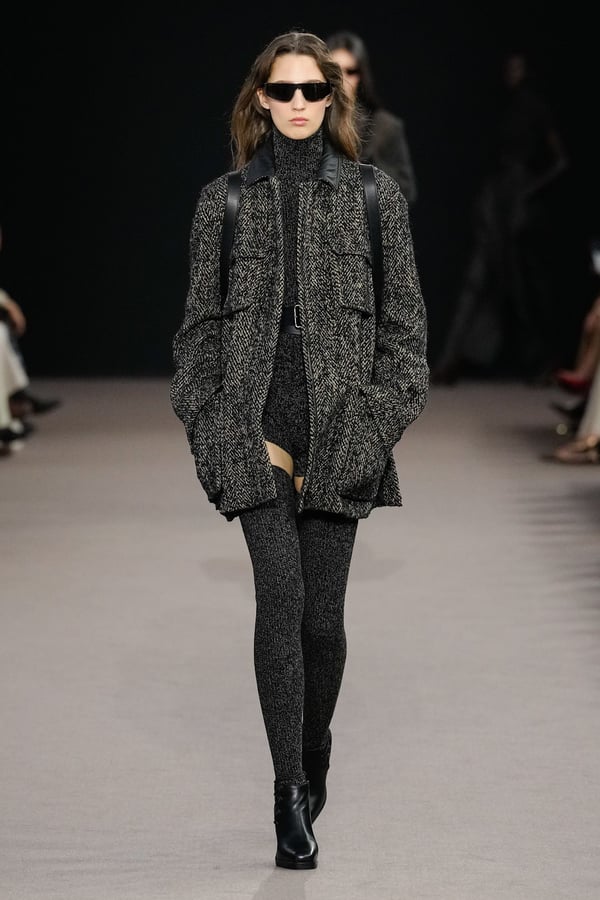 Model wearing a herringbone tweed jacket with a black knit turtleneck, leggings and ankle boots