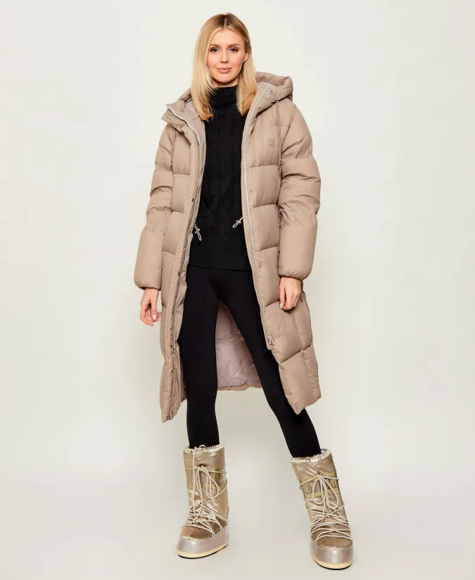 Woman in beige long puffer coat, black turtleneck, black leggings and moon boots