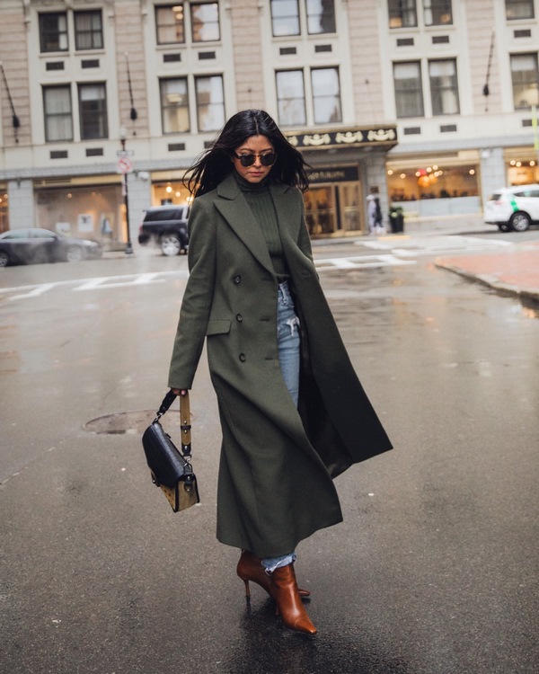 Woman in an olive green coat with jeans and boots