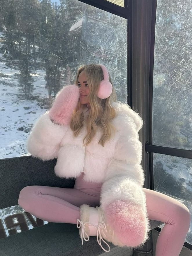 Woman in cream and pink moon boots, white faux-fur jacket, pink leggings and pink earmuffs in a gondola