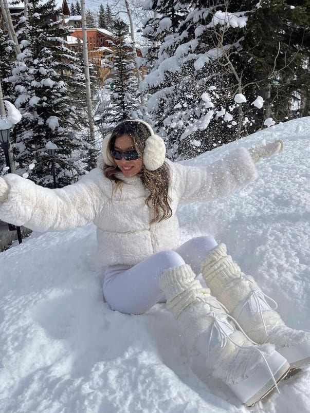 Woman in cream moon boots, white shearling-look puffer and white leggings playing in snow