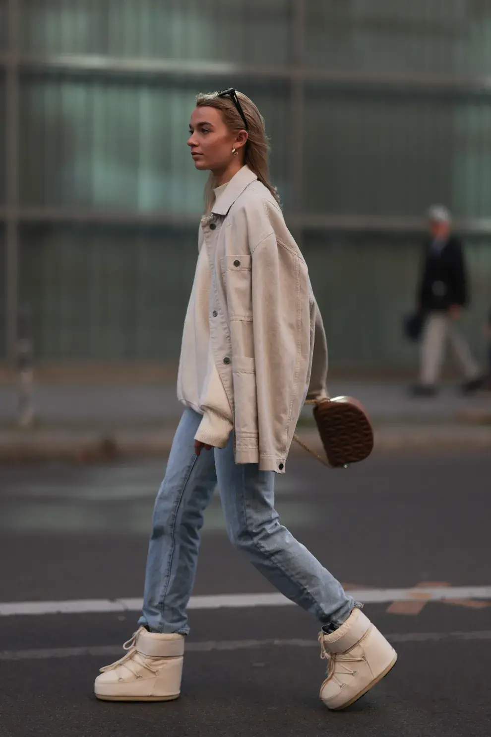 Woman in cream moon boots, light blue jeans and a cream overshirt jacket walking on a city street