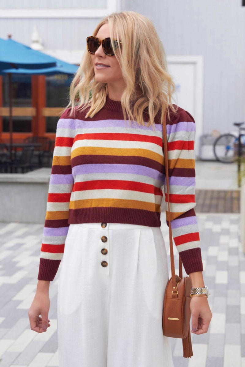 Woman wearing a colorful multi-stripe knit sweater with white jeans