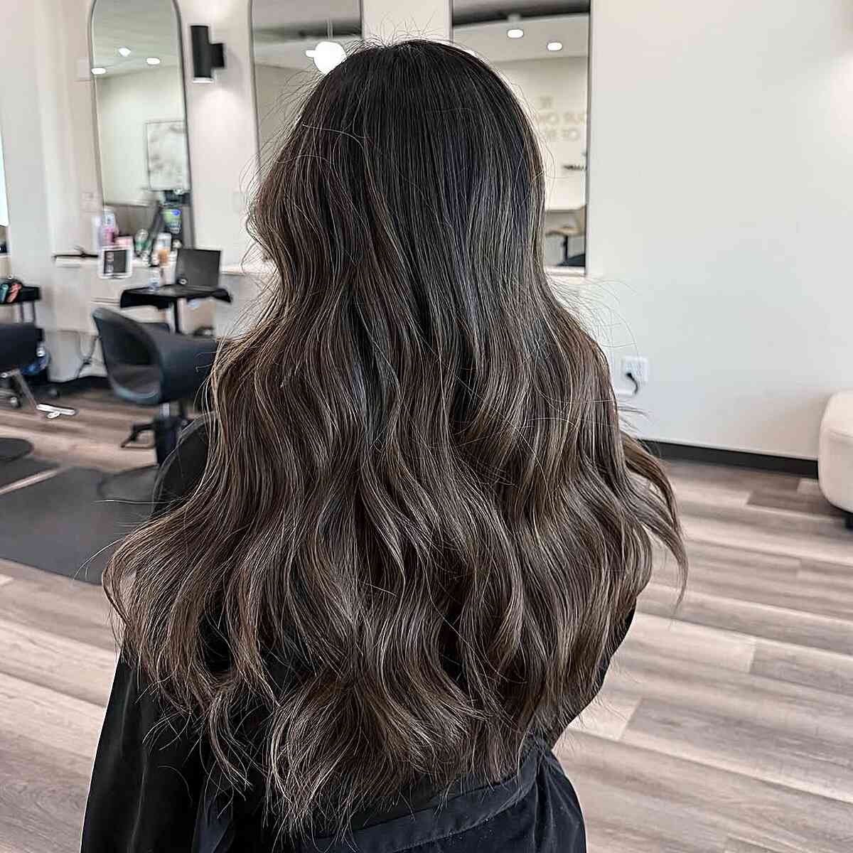 Back view of long wavy hair with soft ash mushroom brown balayage in a salon