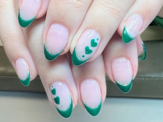 Almond nails with sheer pink base, emerald French tips, glitter edge and green heart accents