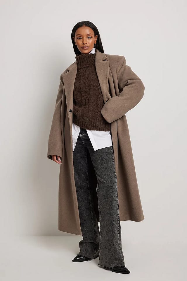 Woman in a white button-down shirt with dark jeans and an oversized coat