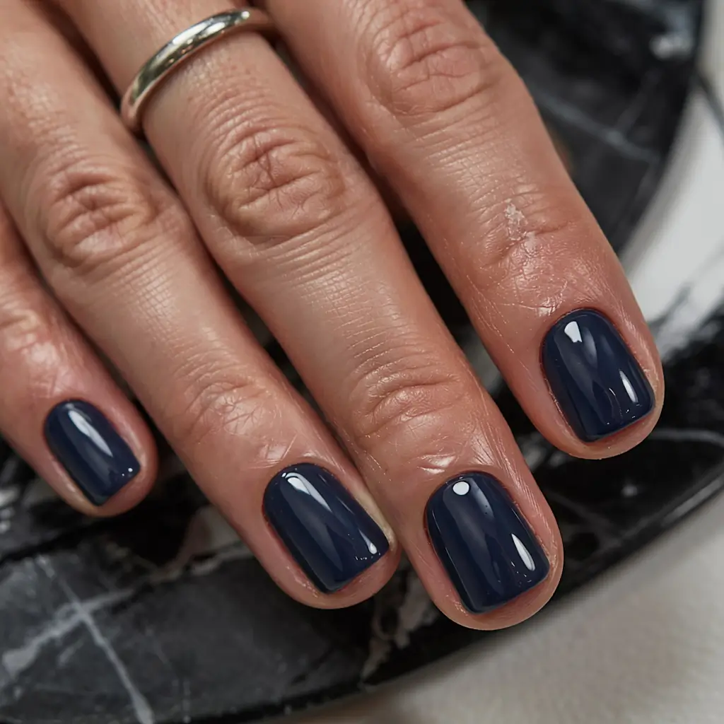 Short squoval nails in a deep glossy midnight-navy crème; real photography.
