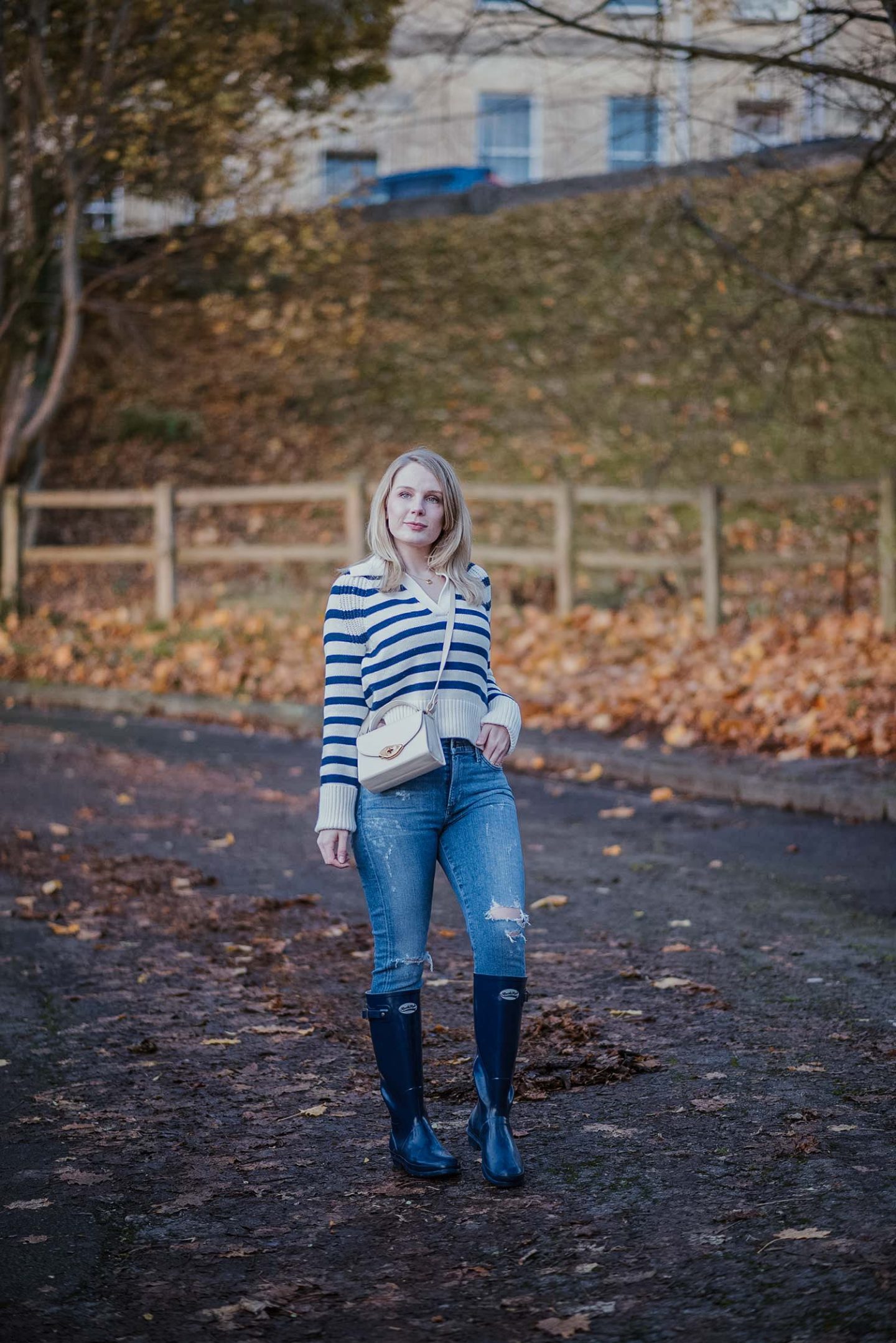 Woman in a navy and white striped sweater with medium-wash jeans, navy wellington boots and a white crossbody bag