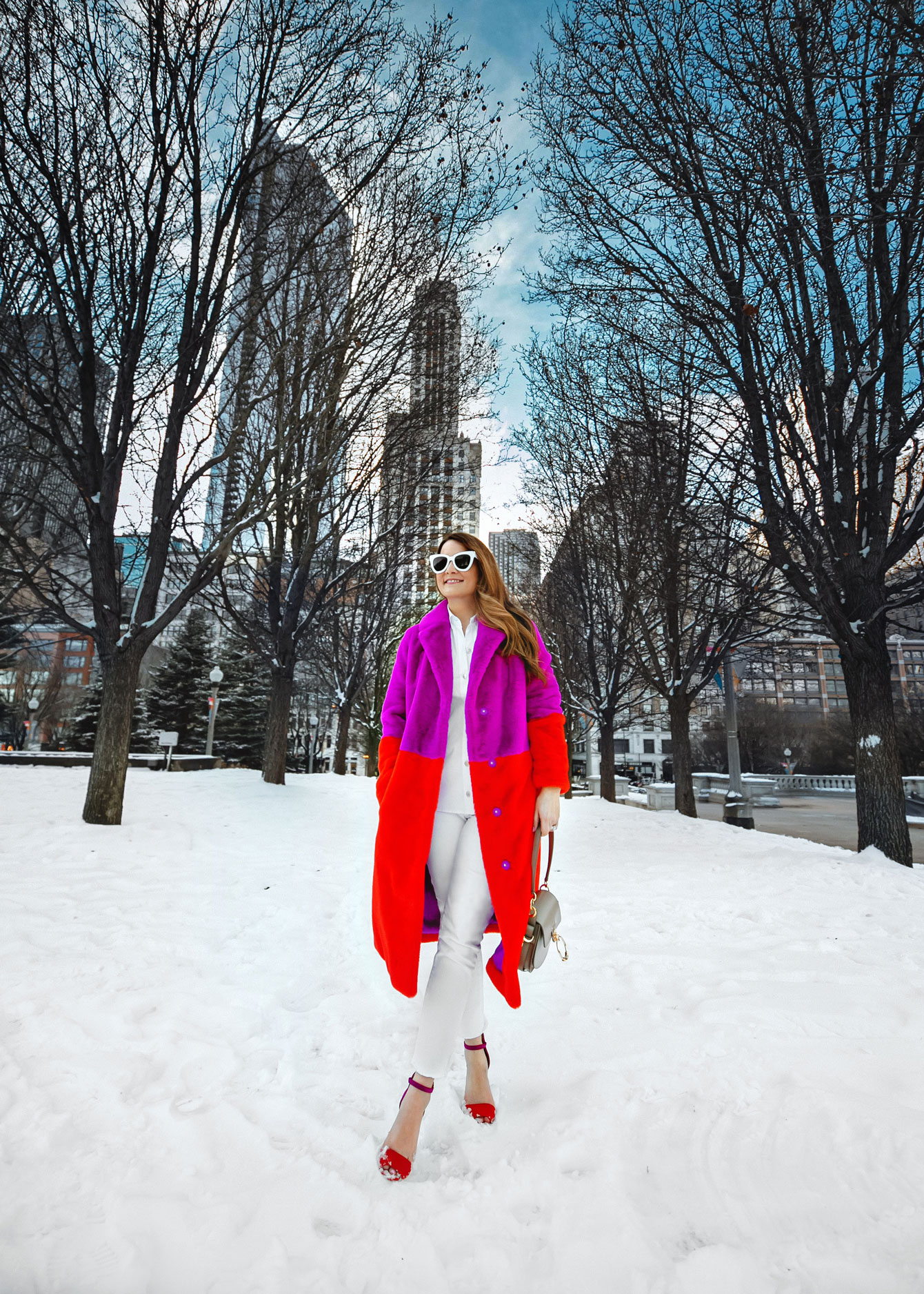 Woman in a magenta and red color-block faux fur coat over a white shirt and white trousers in the snow