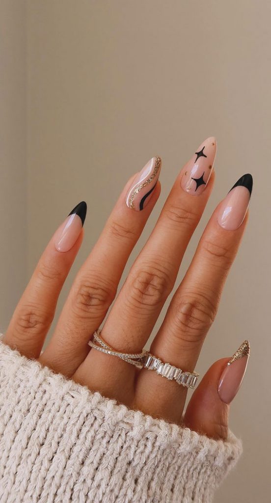 Nude almond nails with alternating black French tips, gold glitter French, and starburst art