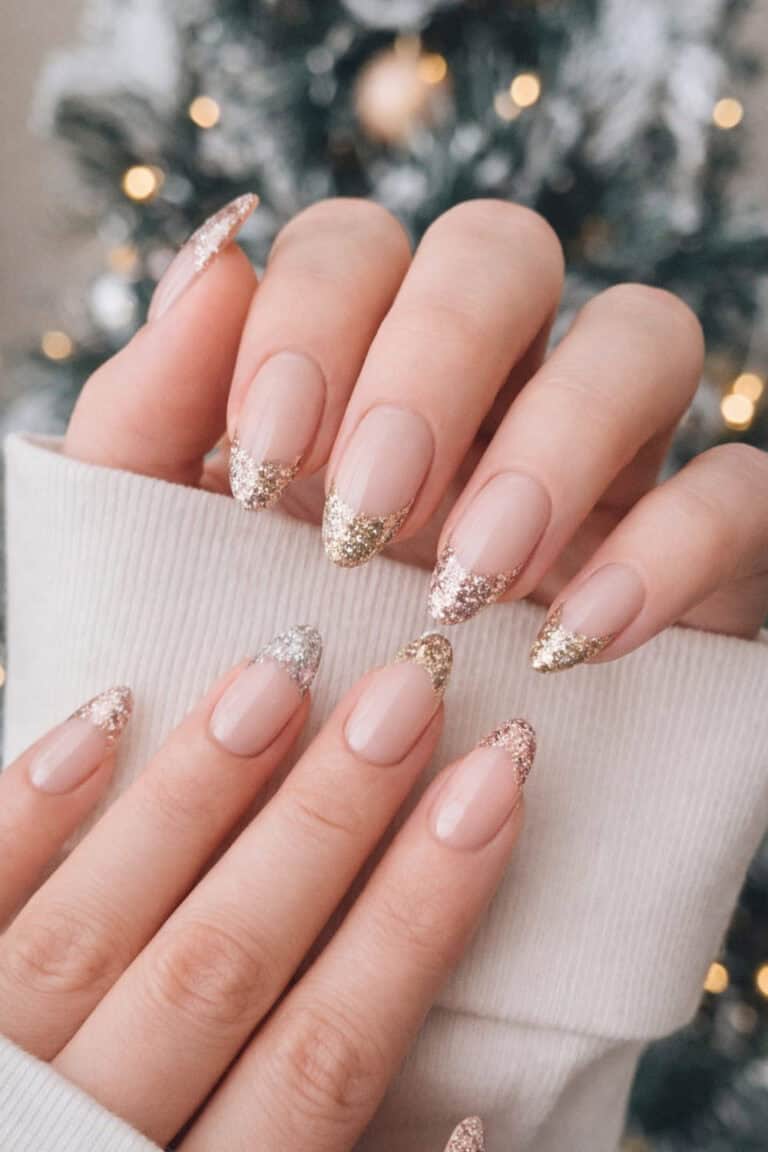 Nude almond nails with gold glitter French tips in front of a Christmas tree