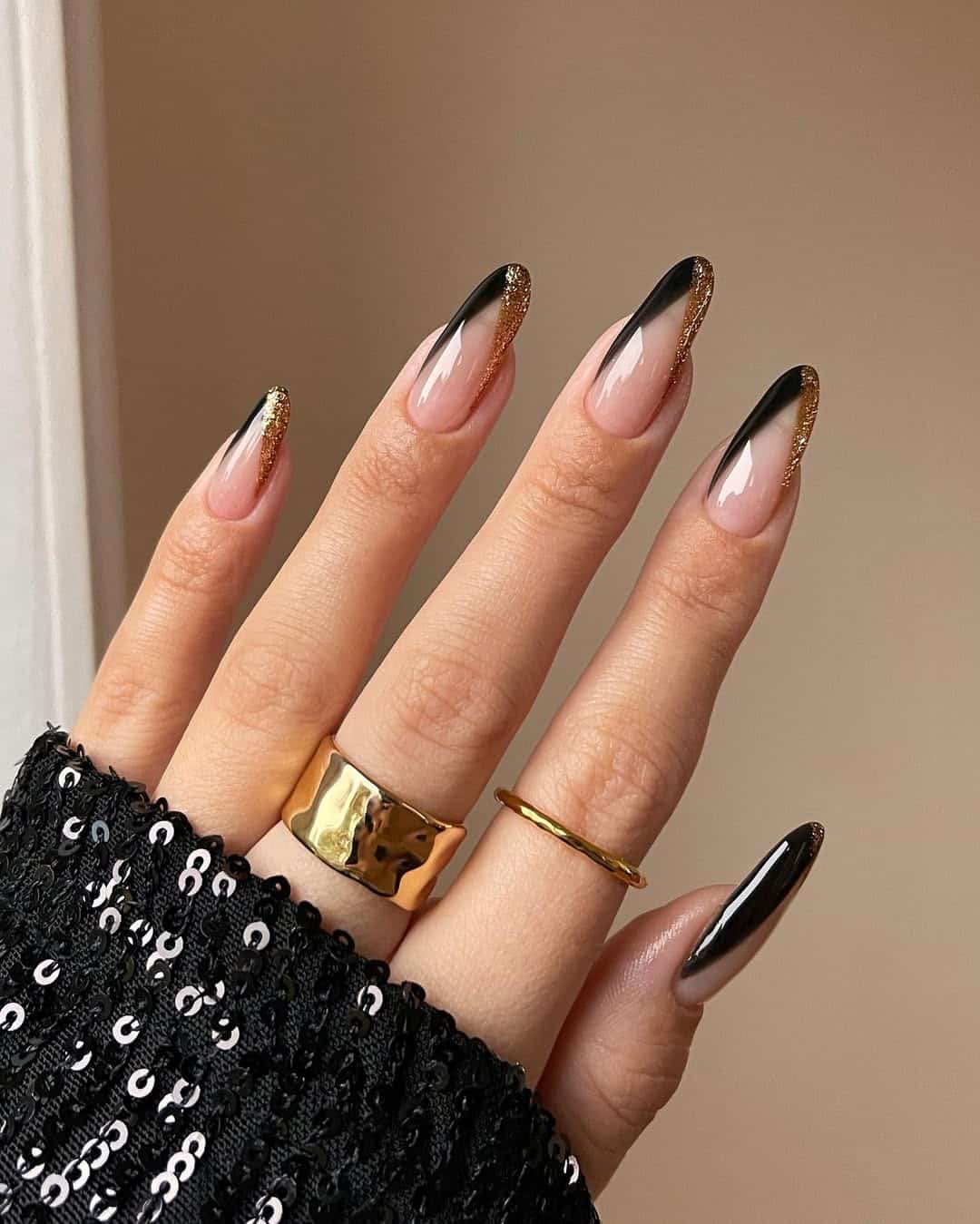 Long almond nails with black French tips melting into gold glitter