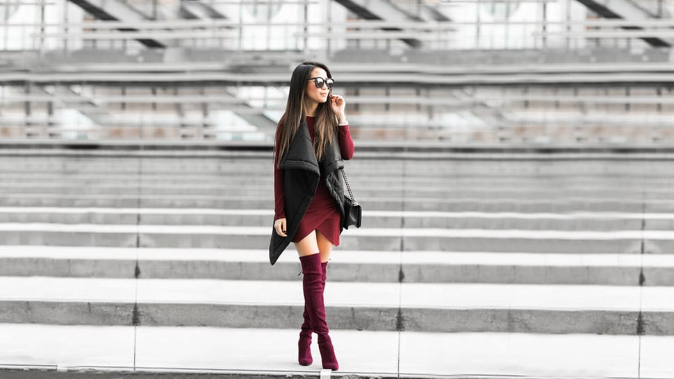 Burgundy over-the-knee boots with a burgundy dress and black puffer vest