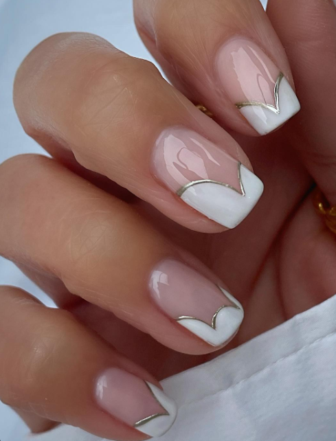 Short squoval nails with a sheer nude-pink base, white French tips, and a thin gold smile line; real photography.