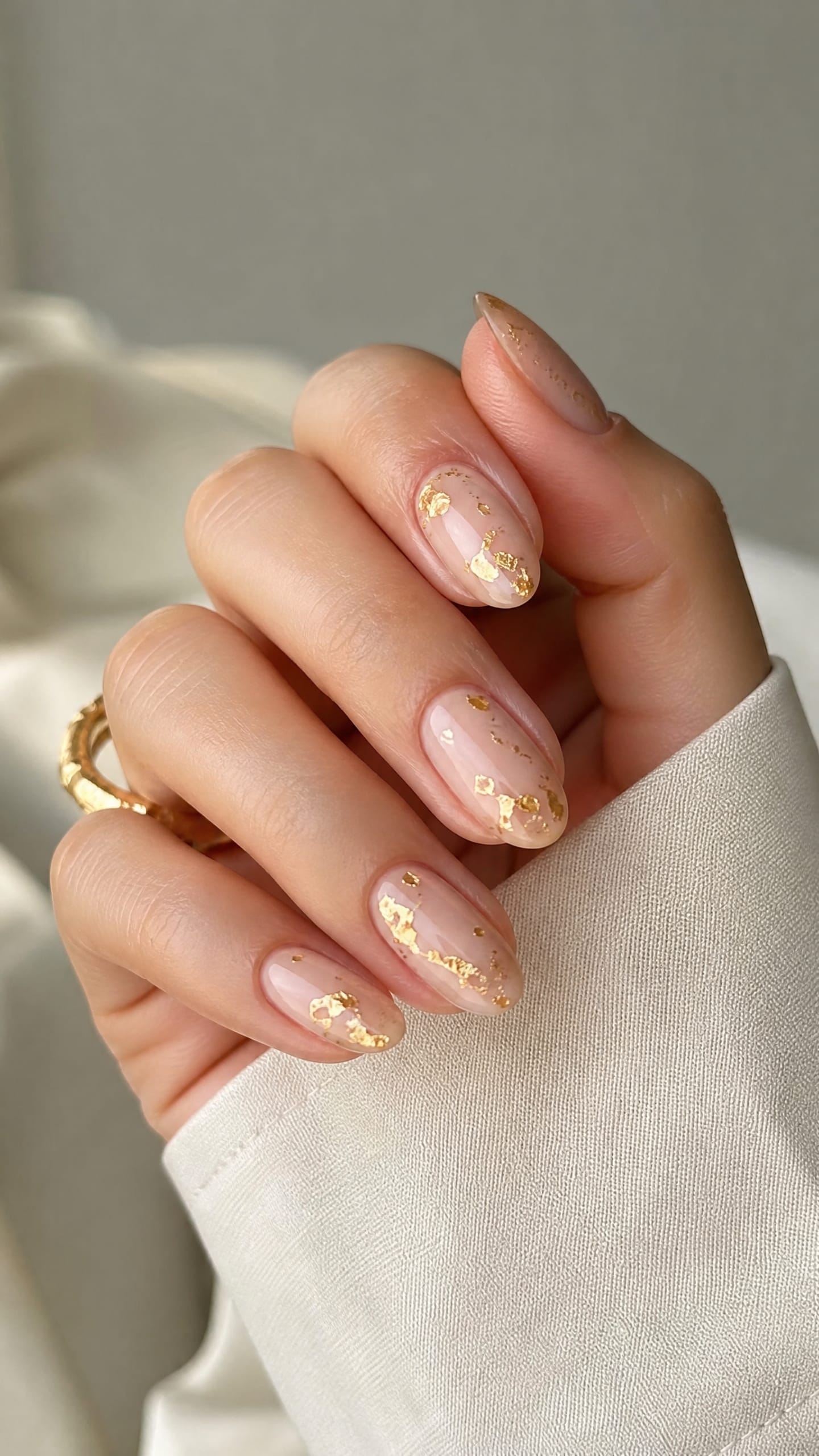 Sheer nude almond nails with small scattered gold foil flakes on each nail.