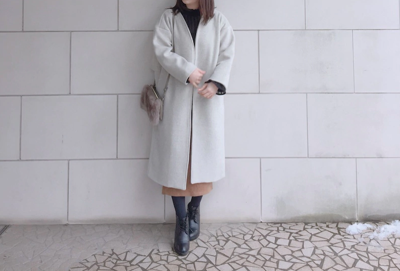 Woman wearing a rust pleated midi skirt with a long cream coat, black tights and lace-up boots