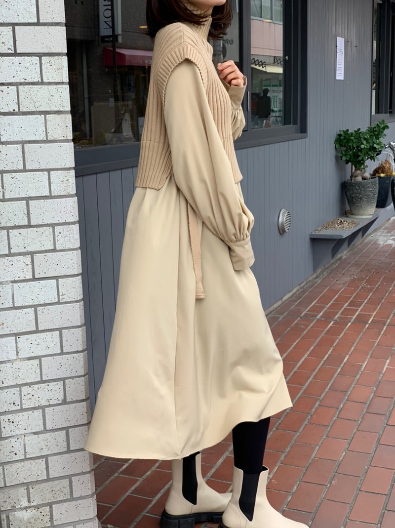 Woman in a beige knit vest layered over a beige blouse with a beige midi skirt, black tights and white Chelsea boots