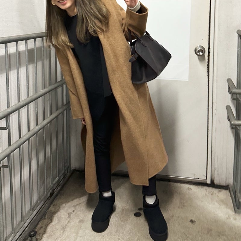 Woman in a camel coat and black outfit wearing black platform mini ugg boots with white socks
