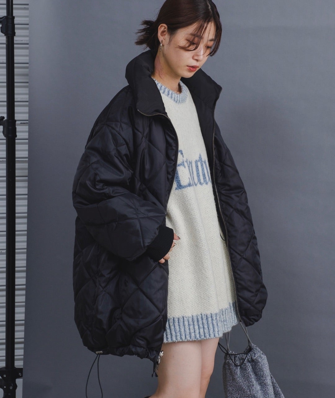 Woman wearing a black quilted coat over a cream knit sweater dress