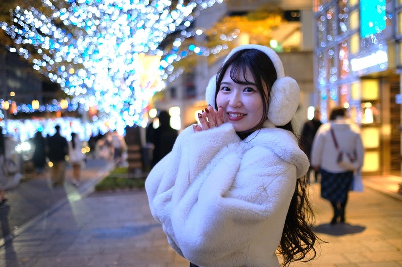 Woman in white earmuffs and a white teddy coat in front of night city illuminations