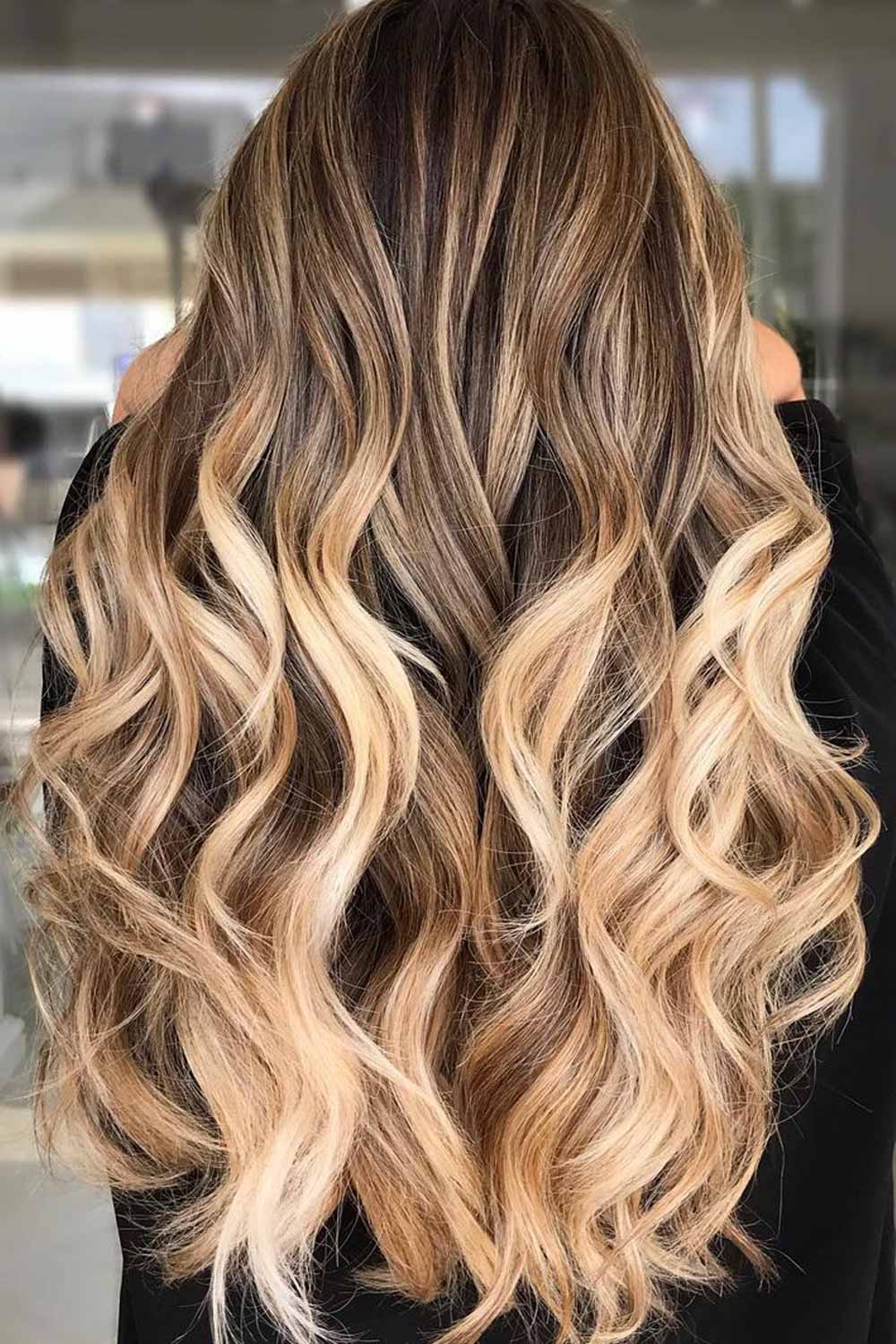 Back view of long wavy hair with medium-brown roots melting into golden honey-blonde ends