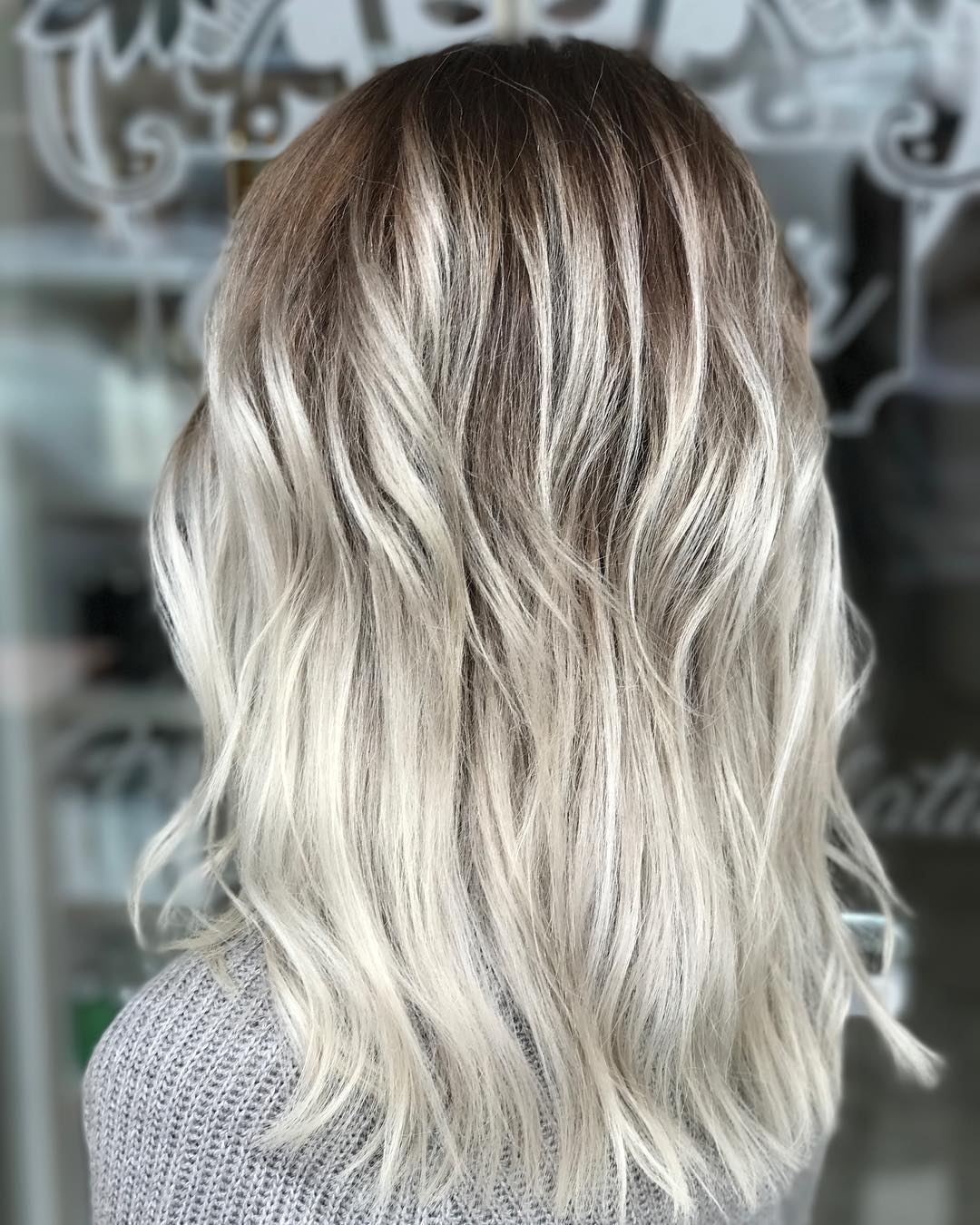Back view of medium-length wavy hair with dark ash-brown roots fading to icy platinum ends