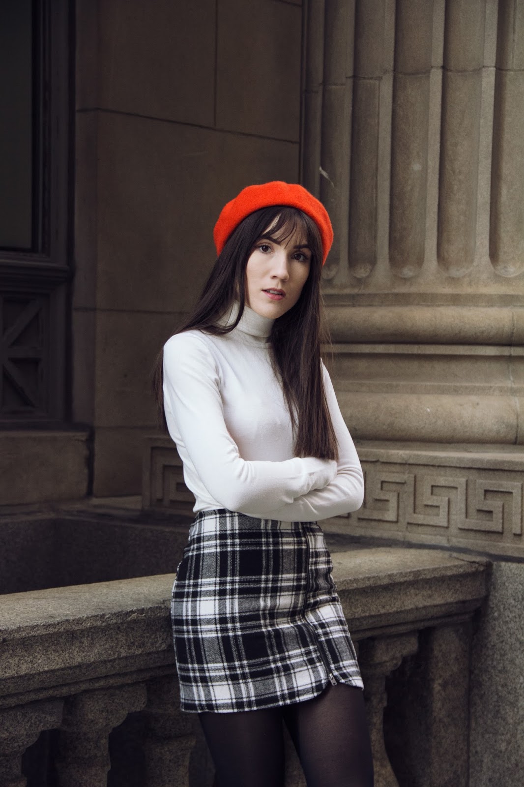 Woman wearing an orange beret with a white turtleneck and plaid mini skirt