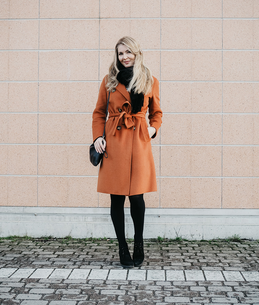 Rust belted wrap coat with a black scarf, black tights, and ankle boots