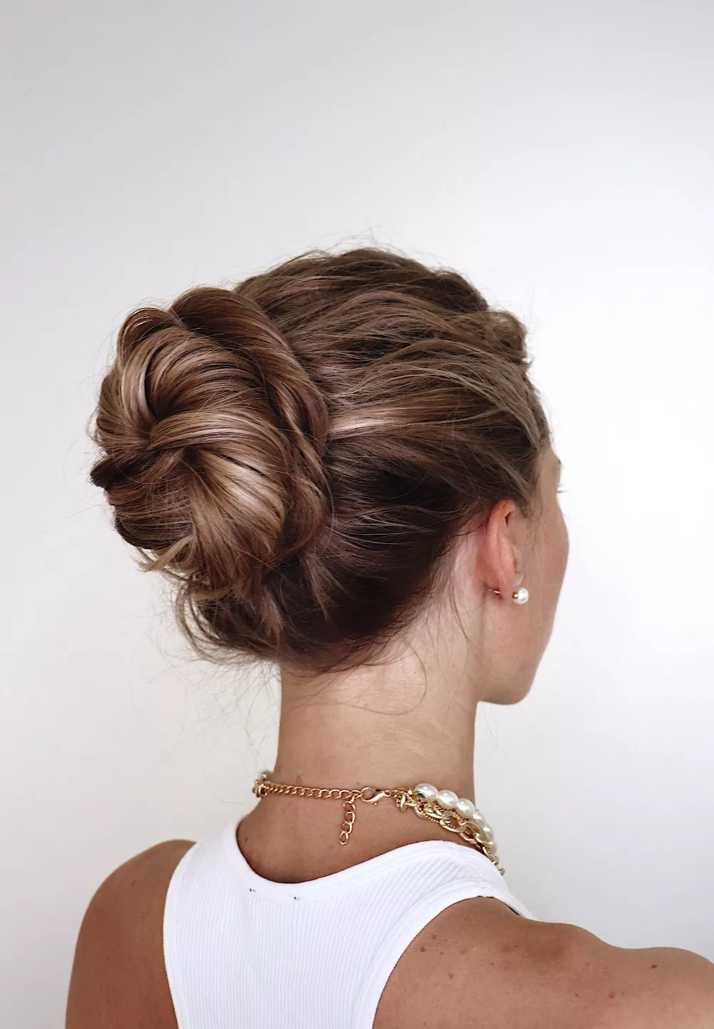 Back view of a messy textured bun with caramel highlights worn high at the crown.